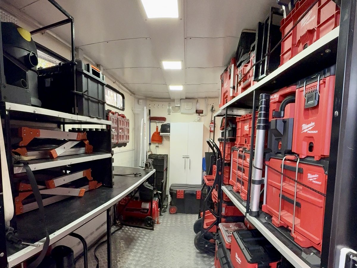 Interior del tráiler: banco de trabajo, compresor y estanterías con herramental y carros de transporte